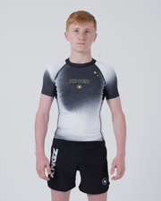 Kingz Galaxy Youth Rashguard Black White - Full Body Front View Teen Boy Athlete Short Sleeve Black White Ombre Galaxy Pattern Gold Star KINGZ Gold Text Crown Logo Black Shorts Kids BJJ