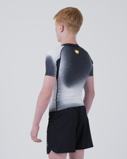 Kingz Galaxy Youth Rashguard Black White - Full Body 3/4 Back View Right Side Teen Boy Athlete Short Sleeve Galaxy Ombre Pattern Gold Crown Logo Upper Back Black Shorts Youth BJJ