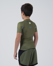 Kingz Trooper Youth Rashguard Military Green - Full Body Back View Young Boy Athlete Short Sleeve Olive Green White Crown Logo Upper Back Dot Pattern Gray Side Panels Black Shorts Kids