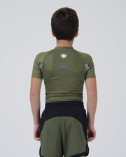 Kingz Trooper Youth Rashguard Military Green - Upper Body Back View Close Young Boy Athlete Short Sleeve Olive Green Crown Logo Back Blue Dot Pattern Gray Panels Black Shorts Kids BJJ