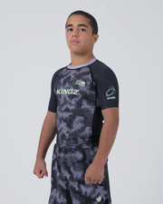 Kingz Viper Youth Rashguard Black Purple - Full Body 3/4 Angled Front View Teen Boy Athlete Short Sleeve Hexagonal Viper Scale Pattern KINGZ Green Text KINGZ Badge Crown Logo Matching Shorts