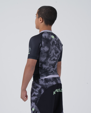 Kingz Viper Youth Rashguard Black Purple - Full Body 3/4 Back View Left Side Teen Boy Athlete Short Sleeve Hexagonal Viper Scale Pattern Green Crown Logo Purple Collar KINGZ Green Text Shorts