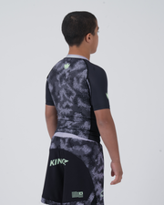 Kingz Viper Youth Rashguard Black Purple - Full Body 3/4 Back View Right Side Teen Boy Athlete Short Sleeve Hexagonal Viper Pattern Green Crown Logo Left Shoulder KINGZ Text Shorts Youth BJJ