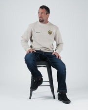 Kingz Jiu Jitsu Club Crewneck - Seated Lifestyle Shot - Model Sitting on Stool - Latte - Men's BJJ Crewneck