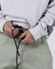Kingz Casual Rip Stop Gi Pant Stone Green - Close-Up Front View Hands Adjusting Black Drawstring Sage Rip Stop Fabric Subtle Grid Pattern BJJ Gi Training [color:Stone Green]