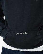 Black BJJ hoodie pocket detail closeup of embroidered jiu jitsu motion cursive script above ribbed hem