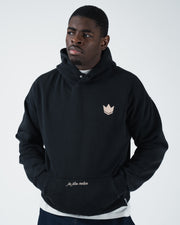 Black BJJ hoodie cropped front view on adult male model with crown logo and hands resting in front pocket
