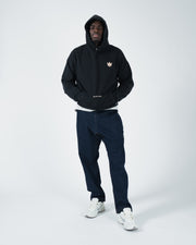 Black BJJ hoodie front view on adult male model with tan crown emblem and layered casual training look