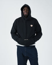 Black BJJ hoodie front view on adult male model wearing hood up with hands tucked in kangaroo pocket