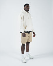 Beige BJJ hoodie full body lifestyle shot with adult male model in matching beige shorts and white shoes