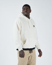 Beige BJJ hoodie cropped front pose on adult male model highlighting dark crown logo and ribbed cuffs