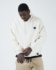 Beige BJJ hoodie lifestyle shot with adult male model looking down adjusting cuff showing crown logo