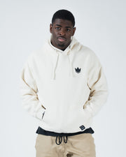 Beige BJJ hoodie cropped front view on adult male model with hands in kangaroo pocket and crown logo