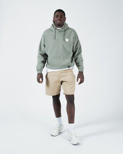 Dark forest green BJJ hoodie full body lifestyle shot with adult male model in beige shorts and sneakers