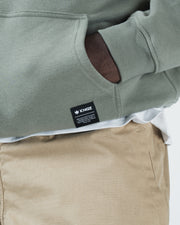 Dark forest green BJJ hoodie bottom hem closeup of woven Kingz crown label tag and kangaroo pocket opening