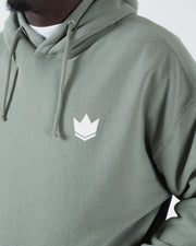 Dark forest green BJJ hoodie chest closeup of white crown emblem logo and drawstring hood cords detail