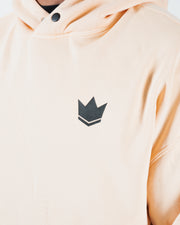 Peach BJJ hoodie chest detail closeup of dark crown logo with snap button collar and soft fleece texture