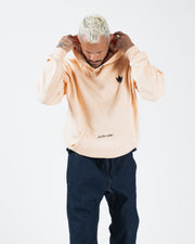 Peach BJJ hoodie lifestyle shot with adult male model adjusting hood with both hands and head lowered