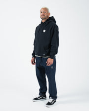 Black BJJ hoodie full body lifestyle shot with adult male model in dark jeans and black sneakers standing