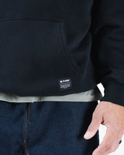 Black BJJ hoodie bottom hem closeup showing woven Kingz crown label tag pocket edge and ribbed hem