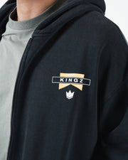 Black BJJ zip up hoodie chest closeup of Kingz flag banner logo and crown emblem beside front zipper
