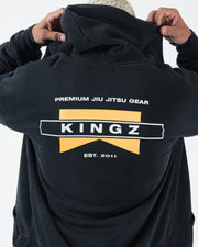 Black BJJ zip up hoodie back view on adult male model raising hood up above the Kingz flag graphic print
