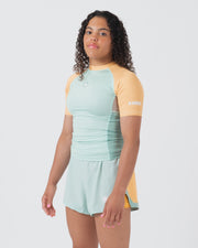 Kingz Terra Women's Rashguard Green Edition - Full Body 3/4 Front Left Side View Female Athlete Short Sleeve Mint Light Green Body Yellow Peach Raglan Sleeves Crown Logo KINGZ White Sleeve Text Matching Mint Hybrid Shorts Women's BJJ
