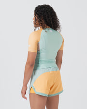 Kingz Terra Women's Rashguard Green Edition - Full Body Back View Female Athlete Short Sleeve Yellow Peach Raglan Sleeves Mint Green Back Panel White Crown Logo Upper Back Matching Hybrid Shorts Yellow Body Mint Trim Women's BJJ
