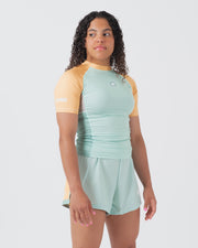 Kingz Terra Women's Rashguard Green Edition - Full Body 3/4 Front Right Side View Female Athlete Short Sleeve Mint Green Body Yellow Peach Raglan Sleeves Crown Logo KINGZ White Left Sleeve Text Matching Mint Hybrid Shorts Terra Collection BJJ