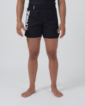 Kingz Kore 2.0 Women's Shorts Black - Full Body Front View Female Athlete Solid Black Bold Vertical KINGZ White Text Left Leg Circular Crown Badge Right Leg Black Elastic Waistband Competition Cut Women's Grappling Shorts No-Gi BJJ [color:Black]