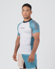 Kingz Flow Rashguard White Teal Blue - Full Body 3/4 Front Right Side View Male Athlete Short Sleeve White Body Teal Raglan Sleeves Wave Pattern Detail KINGZ Pink Text Matching Two-Tone Shorts Flow Design BJJ