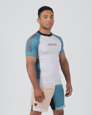 Kingz Flow Rashguard White Teal Blue - Full Body 3/4 Front Left Side View Male Athlete Short Sleeve White Body Teal Raglan Sleeves Wave Pattern KINGZ Pink Text Chest Matching Two-Tone Shorts Teal Blue Panels BJJ