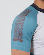 Kingz Flow Rashguard White Teal Blue - Close Up Sleeve Detail Teal Blue Panel Wave Flow Pattern KINGZ KIMONOS Pink Text Lower Sleeve Dark Navy Collar Sublimated Graphics Lightweight Poly Spandex Construction