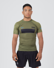 Kingz Trooper Rashguard Military Green - Full Body Front View Male Athlete Short Sleeve Olive Green Black Chest Band KINGZ Text Flag Patch Blue Dot Pattern Sleeves Gray Side Panels Shorts
