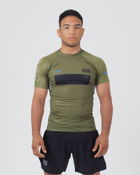 Kingz Trooper Rashguard Military Green - Full Body Front View Male Athlete Short Sleeve Olive Green Black Chest Band KINGZ Text Flag Patch Blue Dot Pattern Sleeves Gray Side Panels Shorts