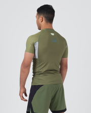 Kingz Trooper Rashguard Military Green - Full Body 3/4 Back View Right Side Male Athlete Short Sleeve Crown Logo Blue Dot Pattern Upper Back Gray Side Panel Black Shorts BJJ Training