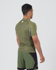 Kingz Trooper Rashguard Military Green - Full Body 3/4 Back View Left Side Male Athlete Short Sleeve Crown Logo Back Blue Dot Detail Gray Side Panels Olive Green Shorts Black Accents
