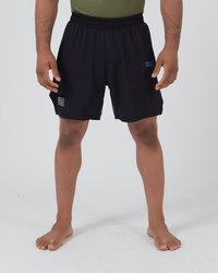Kingz Trooper Hybrid Shorts Black Olive - Full Body Front View Male Athlete Solid Black Outer Shell Olive Green Inner Compression Shorts Visible Blue KINGZ Badge Right Thigh Circular Crown Badge Flag Badge Left Leg Tactical Military Aesthetic Men's Grappling Shorts