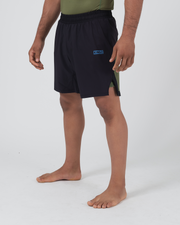 Kingz Trooper Hybrid Shorts Black Olive - Full Body Right Side Profile Male Athlete Solid Black Outer Shell KINGZ Blue Text Badge Front Right Thigh Olive Green Side Panel Visible Men's Grappling Shorts No-Gi BJJ