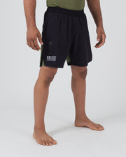 Kingz Trooper Hybrid Shorts Black Olive - Full Body Left Side Profile Male Athlete Solid Black Front Panel Crown Badge Flag Badge Graphic Left Leg Olive Green Side Panel Visible Inner Compression Shorts Men's Grappling Shorts No-Gi BJJ