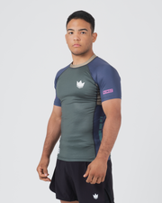 Kingz Draft Rashguard Storm Blue - Full Body 3/4 Angled Front View Male Athlete Short Sleeve Gray Body Blue Raglan Sleeves Crown Logo Pink KINGZ Sleeve Label Black Shorts Crown Badge