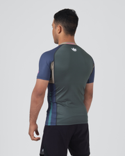 Kingz Draft Rashguard Storm Blue - Full Body 3/4 Back View Left Side Male Athlete Short Sleeve Gray Body Crown Logo Upper Back Blue Raglan Sleeves Teal Side Stripe Pink KINGZ Label Shorts