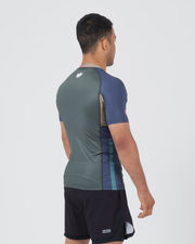 Kingz Draft Rashguard Storm Blue - Full Body 3/4 Back View Right Side Male Athlete Short Sleeve Crown Logo Back Blue Raglan Sleeves Teal Side Stripes Gray Body KINGZ Badge Shorts