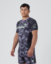 Kingz Viper Rashguard Black Purple - Full Body 3/4 Front Right Side View Male Athlete Short Sleeve Hexagonal Viper Scale Pattern Dark Gray Purple Collar Green Crown Logo KINGZ Sleeve Logo Matching Shorts