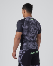 Kingz Viper Rashguard Black Purple - Full Body 3/4 Back Left Side View Male Athlete Short Sleeve Hexagonal Viper Scale Pattern Dark Gray Black Raglan Sleeves Green Crown Logo Back Matching Patterned Shorts KINGZ Green Text