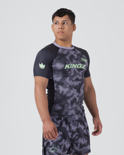 Kingz Viper Rashguard Black Purple - Full Body Front View Male Athlete Short Sleeve Hexagonal Viper Scale Camo Pattern KINGZ Green Chest Text Green Crown Logo Left Sleeve Black Raglan Sleeves Purple Collar Matching Patterned Shorts