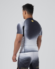 Kingz Galaxy Rash Guard Black White - Full Body Back View Male Athlete Short Sleeve Black To White Ombre Galaxy Pattern Gold Crown Logo Center Back Matching Galaxy Spats Leggings KINGZ Gold Text Bottom BJJ MMA