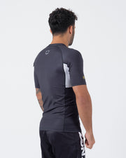Kingz Ranked Performance V2 S/S Rashguard Dark Charcoal White - Full Body 3/4 Back Left Side View Male Athlete Short Sleeve Crown Logo Upper Back White Side Panel Gold IBJJF Cuff KINGZ Shorts Text BJJ Competition Performance