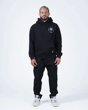 Black BJJ hoodie full body lifestyle shot with adult male model in matching black joggers and sneakers