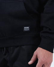 Black BJJ hoodie bottom hem closeup showing woven Kingz premium crafted gear label tag and ribbed hem